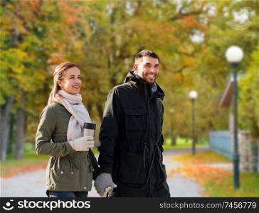 love, relationship and season concept - smiling couple with tumbler walking over autumn park background. couple with tumbler walking along autumn park