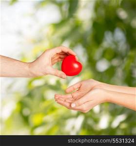 love, relationship, charity and medicine concept - man hand giving red heart to woman