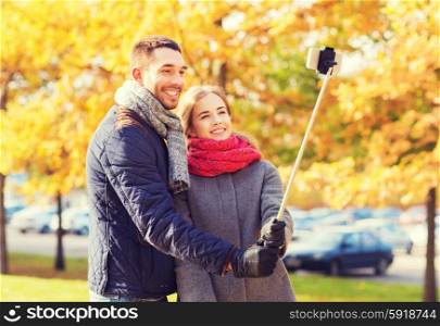 love, relationship, family and people concept - smiling couple hugging and taking selfie with smartphone and monopod in autumn park