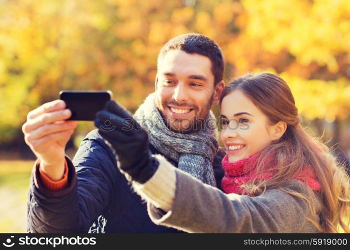 love, relationship, family and people concept - smiling couple hugging and taking selfie with smartphone in autumn park