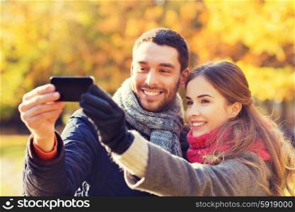 love, relationship, family and people concept - smiling couple hugging and taking selfie with smartphone in autumn park