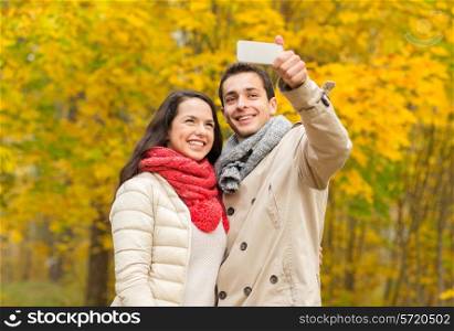 love, relationship, family and people concept - smiling couple hugging and taking selfie in autumn park