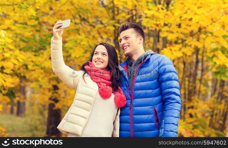 love, relationship, family and people concept - smiling couple hugging and taking selfie in autumn park