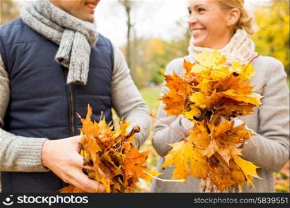 love, relationship, family, season and people concept - close up of happy smiling couple with pile of maple leaves having fun in autumn park