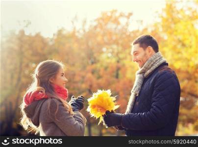 love, relationship, family, season and people concept - smiling couple with bunch of leaves in autumn park
