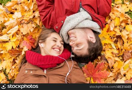 love, relationship, season, family and people concept - close up of happy couple with earphones listening to music and lying on autumn leaves
