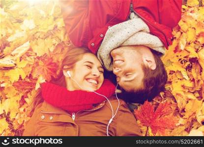 love, relationship, season, family and people concept - close up of happy couple with earphones listening to music and lying on autumn leaves. close up of smiling couple lying in autumn park