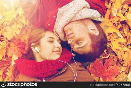 love, relationship, season, family and people concept - close up of happy couple with earphones listening to music and lying on autumn leaves. close up of smiling couple lying in autumn park