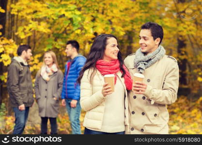 love, relationship, season, friendship and people concept - group of smiling men and women walking with paper coffee cups in autumn park