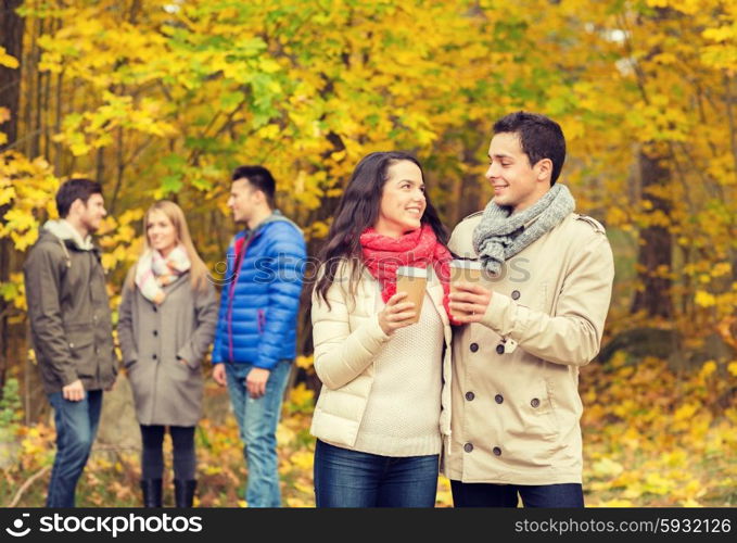 love, relationship, season, friendship and people concept - group of smiling men and women walking with paper coffee cups in autumn park