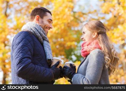love, relationship, season, friendship and people concept - smiling couple with coffee cups in autumn park