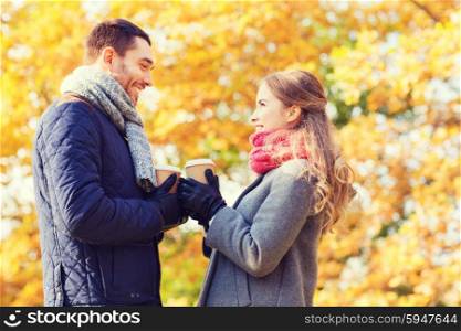 love, relationship, season, friendship and people concept - smiling couple with coffee cups in autumn park