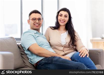 love, relationships and people concept - happy couple sitting on sofa at home. happy couple sitting on sofa at home