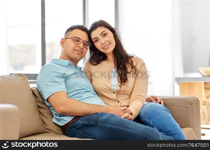 love, relationships and people concept - happy couple sitting on sofa at home. happy couple sitting on sofa at home