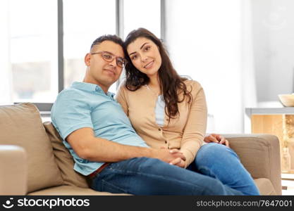 love, relationships and people concept - happy couple sitting on sofa at home. happy couple sitting on sofa at home