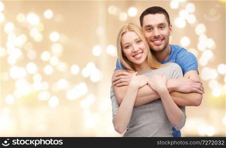 love, relationships and people concept - smiling couple hugging over beige background with festive lights. smiling couple hugging over festive lights