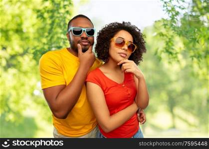love, relationships and summer concept - african american couple in sunglasses thinking over green natural background. african couple in sunglasses thinking