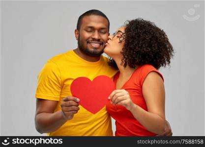 love, relationships and valentines day concept - happy african american couple holding big red paper heart and kiss over grey background. happy african american couple wit red heart kiss