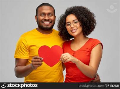 love, relationships and valentines day concept - happy african american couple holding big red paper heart over grey background. happy african american couple holding red heart