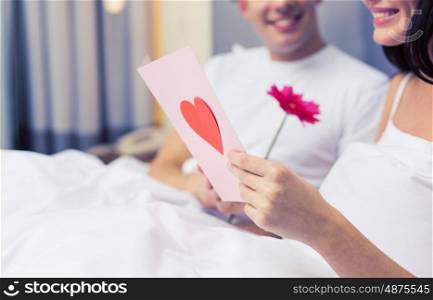 love, relationships, holidays, valentines day and people concept - close up of happy couple in bed with postcard and flower
