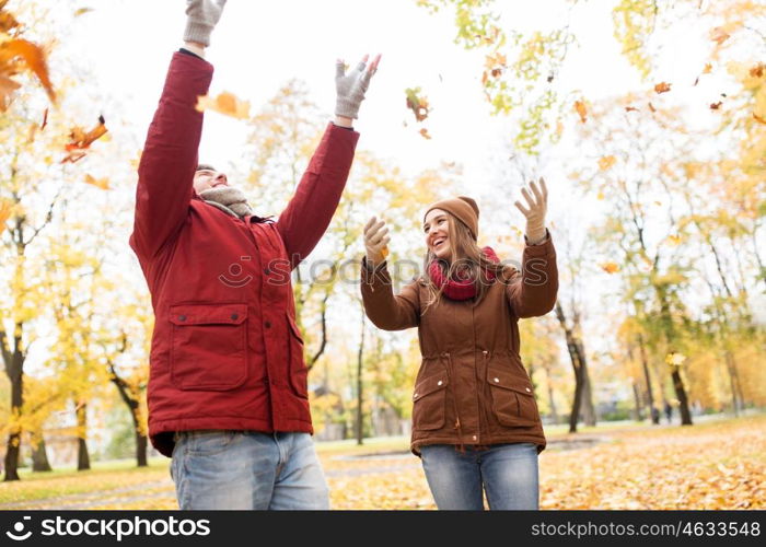 love, relationships, season and people concept - happy young couple throwing autumn leaves up in park