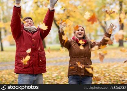 love, relationships, season and people concept - happy young couple throwing autumn leaves up in park