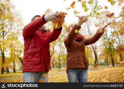 love, relationships, season and people concept - happy young couple throwing autumn leaves up in park