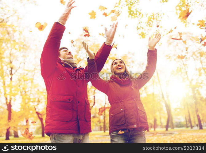 love, relationships, season and people concept - happy young couple throwing autumn leaves up in park. happy young couple throwing autumn leaves in park