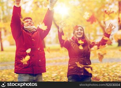 love, relationships, season and people concept - happy young couple throwing autumn leaves up in park. happy young couple throwing autumn leaves in park