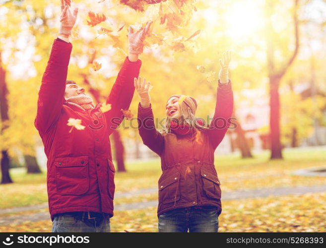 love, relationships, season and people concept - happy young couple throwing autumn leaves up in park. happy young couple throwing autumn leaves in park