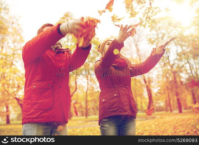 love, relationships, season and people concept - happy young couple throwing autumn leaves up in park. happy young couple throwing autumn leaves in park