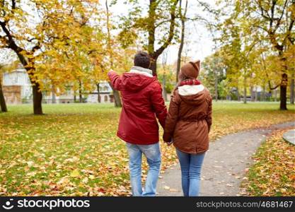 love, relationships, season and people concept - happy young couple walking in autumn park and pointing finger to something