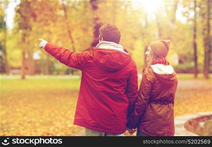 love, relationships, season and people concept - happy young couple walking in autumn park and pointing finger to something. happy young couple walking in autumn park