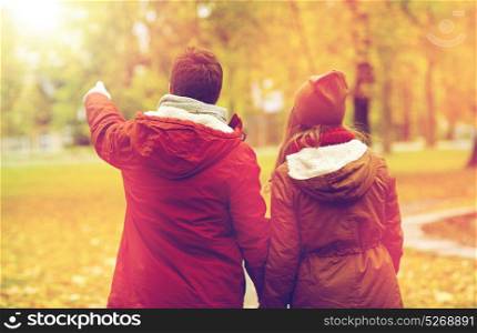 love, relationships, season and people concept - happy young couple walking in autumn park and pointing finger to something. happy young couple walking in autumn park