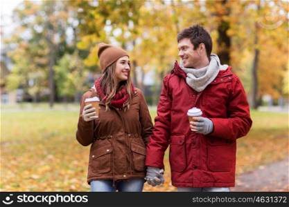love, relationships, season and people concept - happy young couple with coffee cups walking in autumn park