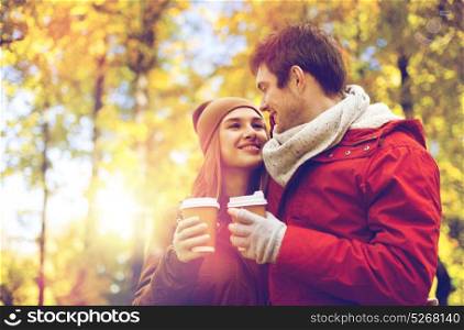 love, relationships, season and people concept - happy young couple with coffee cups walking in autumn park. happy couple with coffee walking in autumn park