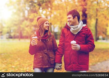 love, relationships, season and people concept - happy young couple with coffee cups walking in autumn park. happy couple with coffee walking in autumn park