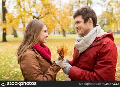 love, relationships, season and people concept - happy young couple with maple leaves in autumn park