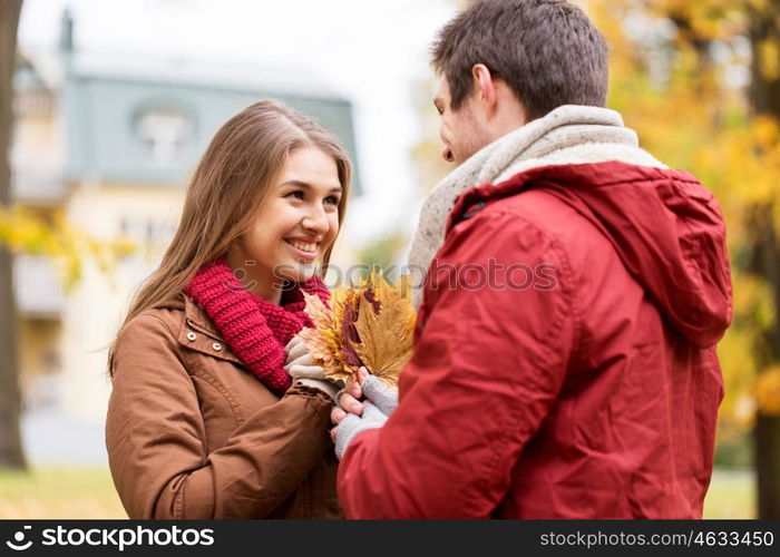 love, relationships, season and people concept - happy young couple with maple leaves in autumn park