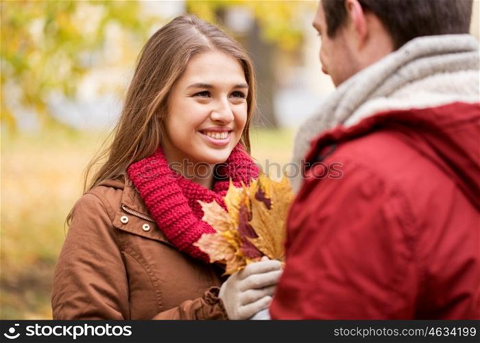 love, relationships, season and people concept - happy young couple with maple leaves in autumn park