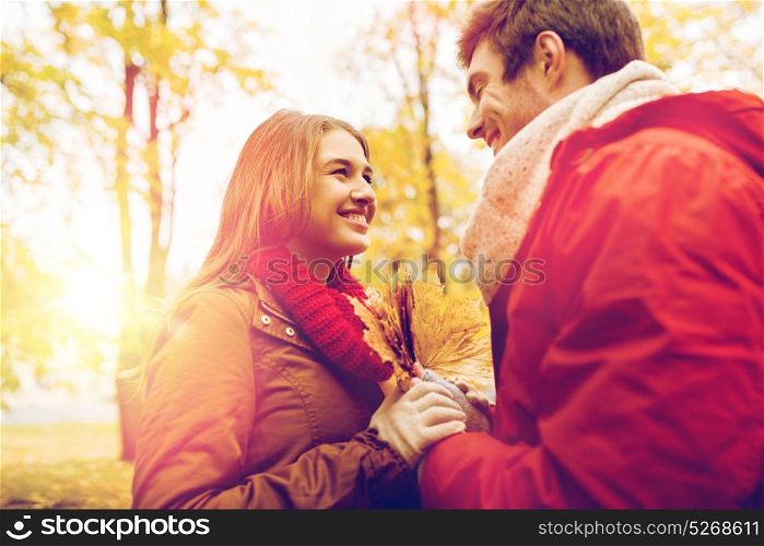 love, relationships, season and people concept - happy young couple with maple leaves in autumn park. happy couple with maple leaves in autumn park