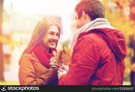 love, relationships, season and people concept - happy young couple with maple leaves in autumn park. happy couple with maple leaves in autumn park