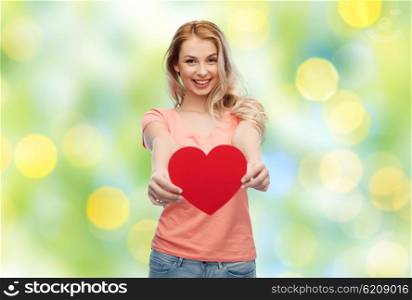 love, romance, charity, valentines day and people concept - smiling young woman or teenage girl with blank red heart shape over summer green lights background