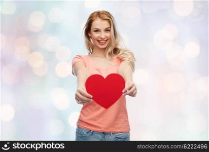 love, romance, charity, valentines day and people concept - smiling young woman or teenage girl with blank red heart shape over blue holidays lights background
