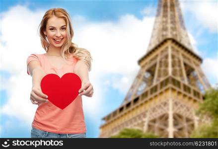love, romance, charity, valentines day and people concept - smiling young woman or teenage girl with blank red heart shape over paris eiffel tower background