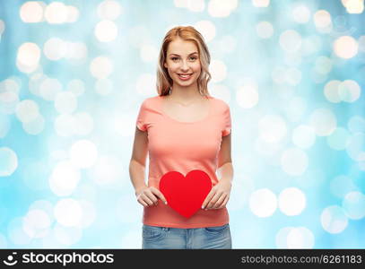 love, romance, charity, valentines day and people concept - smiling young woman or teenage girl with blank red heart shape over blue holidays lights background