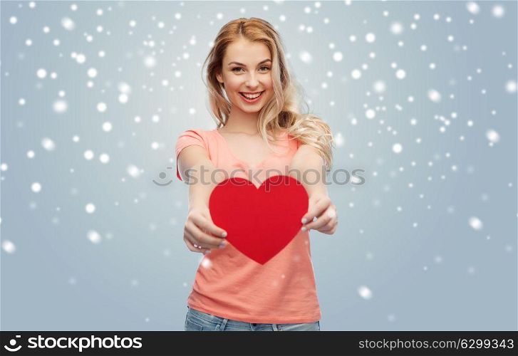 love, romance, charity, valentines day and people concept - smiling young woman or teenage girl with blank red heart shape over gray background and snow. happy woman or teen girl with red heart shape