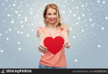 love, romance, charity, valentines day and people concept - smiling young woman or teenage girl with blank red heart shape over gray background and snow. happy woman or teen girl with red heart shape