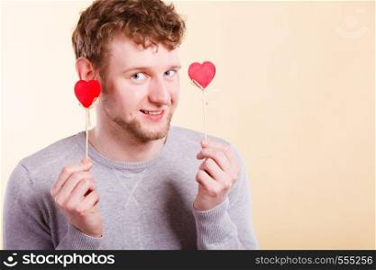 Love romance concept. Happy man holding hearts. Young smiling male holding small items on pole. . Happy man holding hearts.