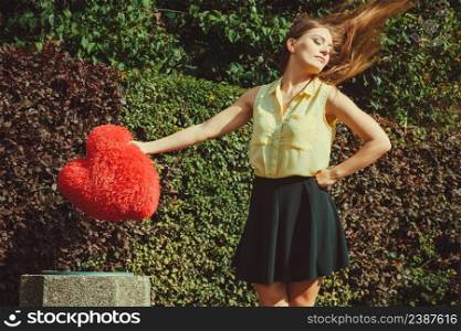 Love romance heartbreak sadness concept. Girl throwing heart into dumpster. Young lady holding plush love symbol over bin.. Girl throwing heart into dumpster.